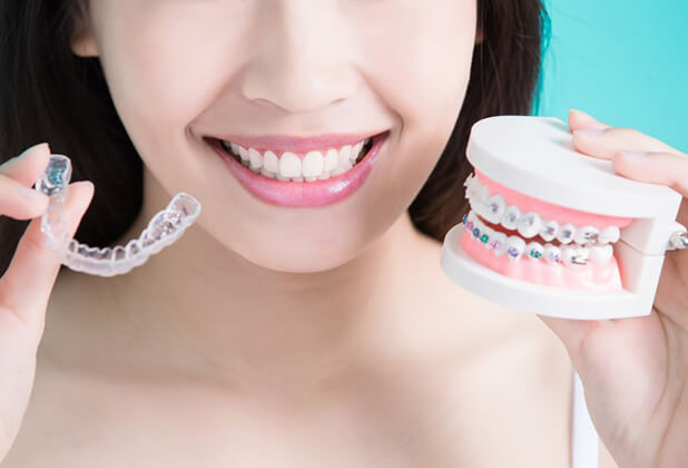person holding an Invisalign® aligner and a model of a mouth with braces