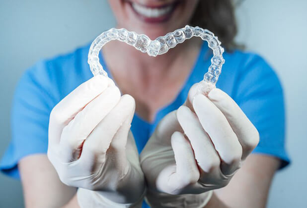 dental hygienist holding two Invisalign® aligners in the shape of a heart