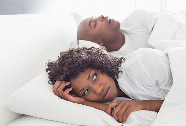 Frustrated woman in bed next to snoring man