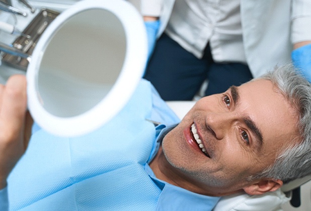 An older man lying back in a dentist’s chair while admiring his veneers during a regular checkup and cleaning